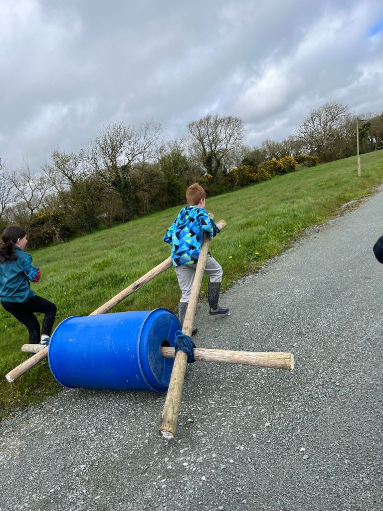 Child pulling blue barrel on sticks along a path.