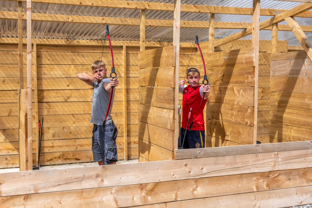 Two people practicing archery in a wooden enclosure.