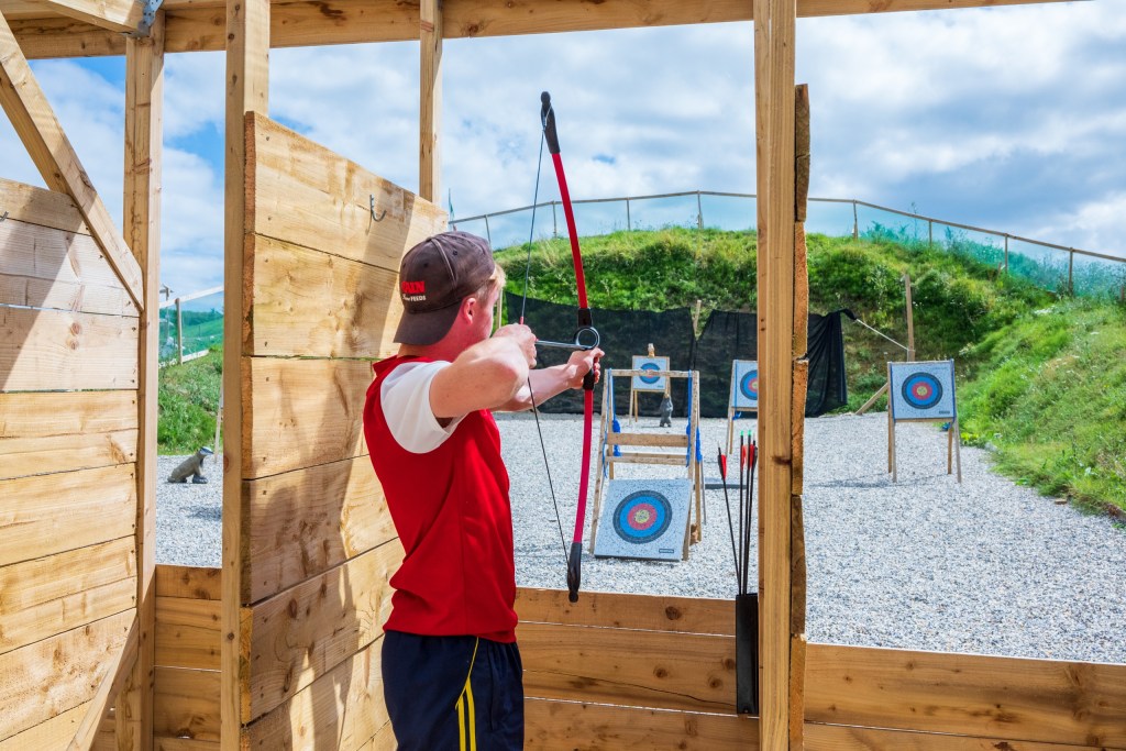 Person in red shirt practicing archery at outdoor range.