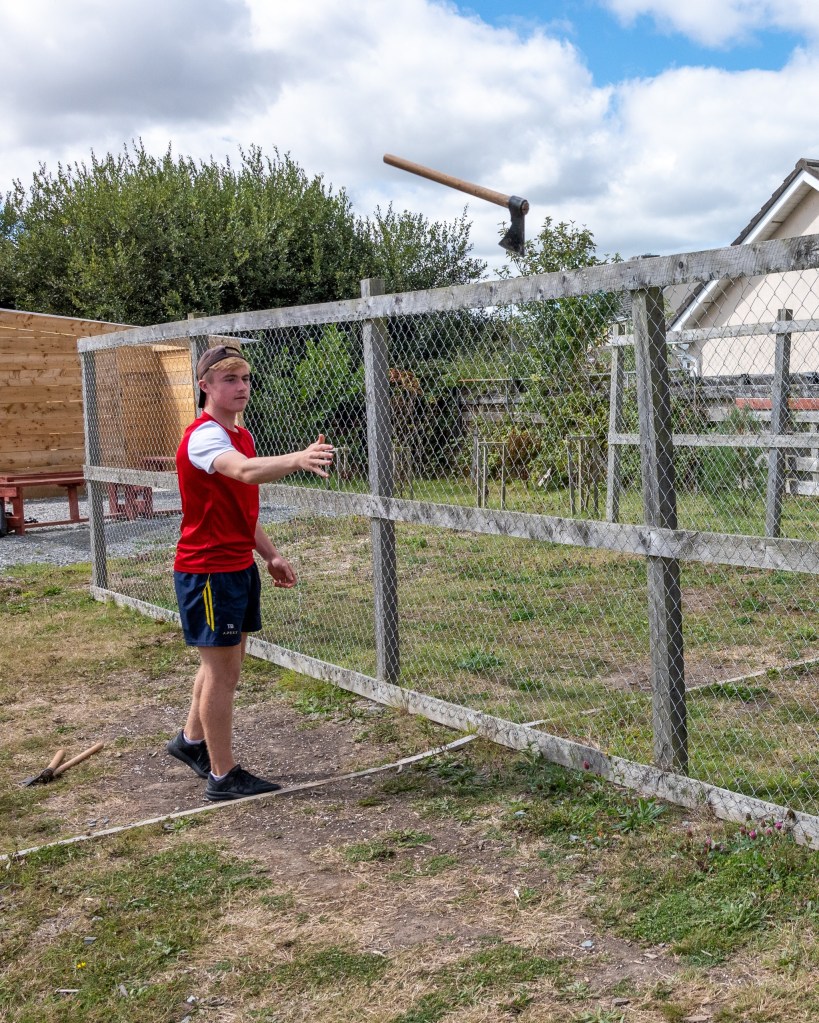 Person in a red shirt playing with a toy near a wire fence on a grassy area.
