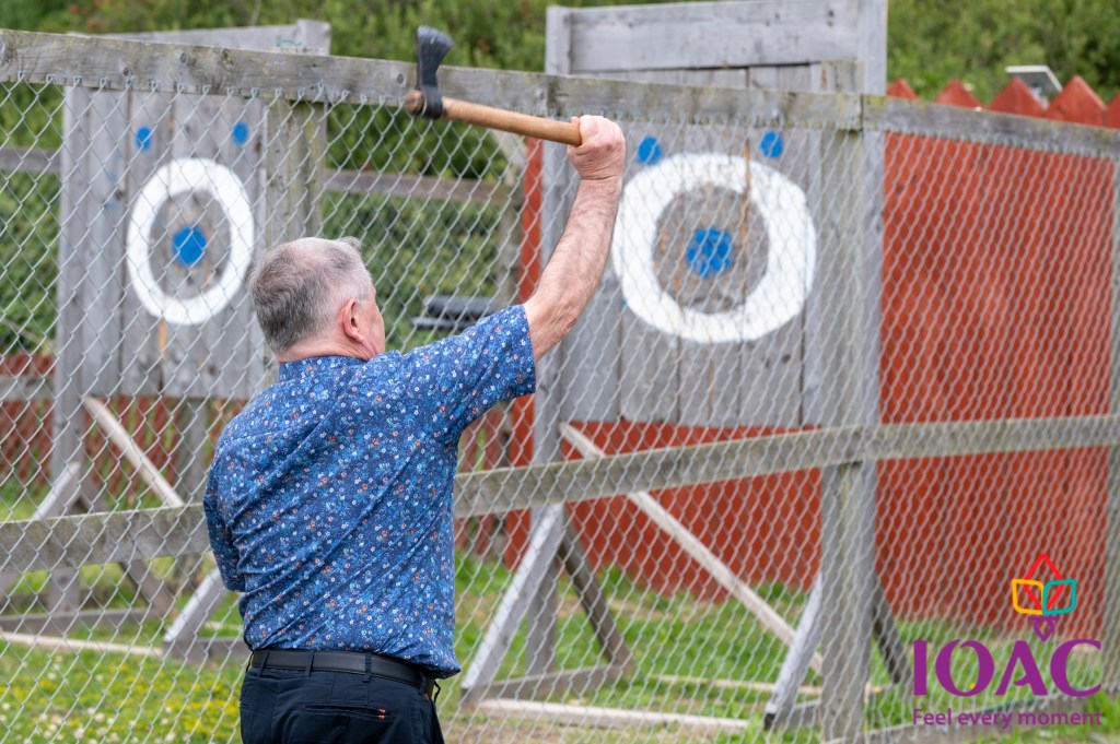 Man preparing to throw axe at wooden target in outdoor range.