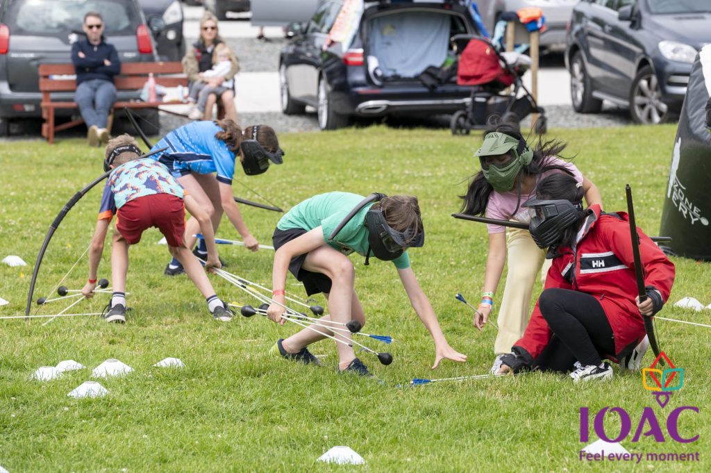 Children playing archery tag on grass with masks and bows.