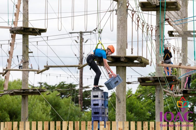 Person stacking crates on a high ropes course wearing a helmet and harness.