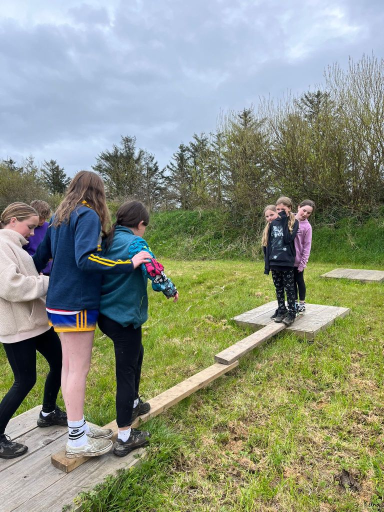 Children balancing on wooden boards in a grassy field under cloudy sky.