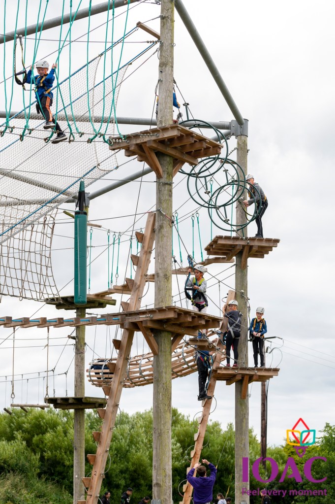 People climbing a tall outdoor ropes course with ladders and platforms.