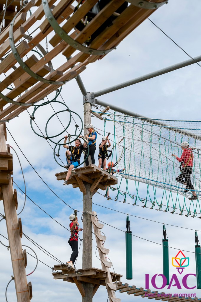 People navigating a wooden and rope obstacle course in the sky.
