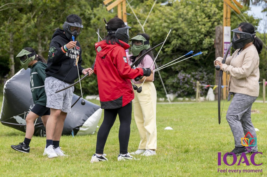 Group playing archery tag with masks and padded arrows outdoors.