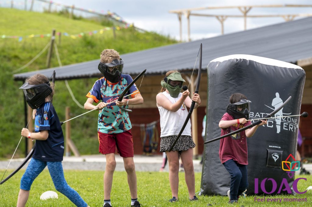 Children playing archery tag outdoors, wearing masks and holding bows.
