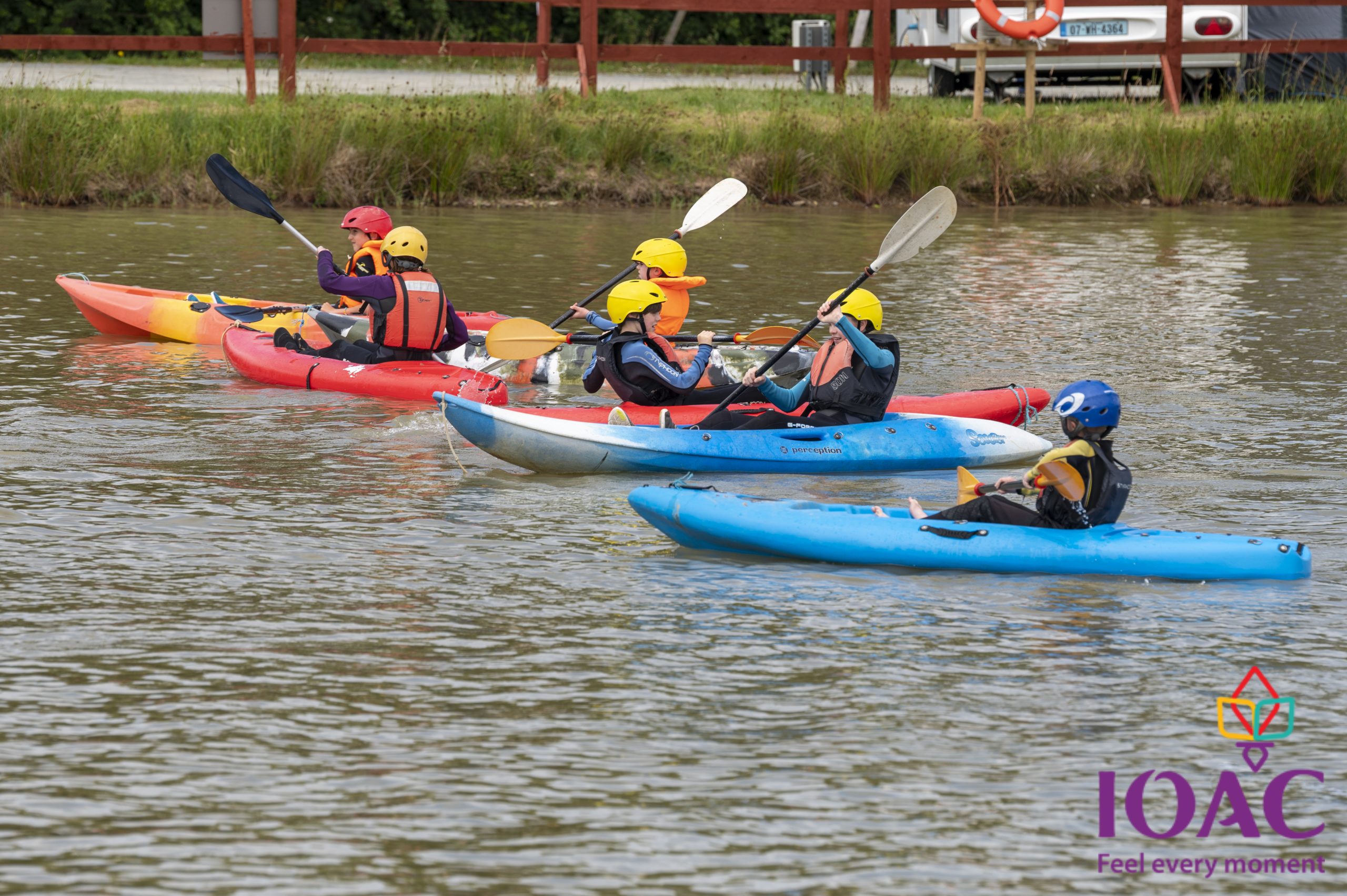 Four people kayaking on a lake, wearing helmets and life jackets.