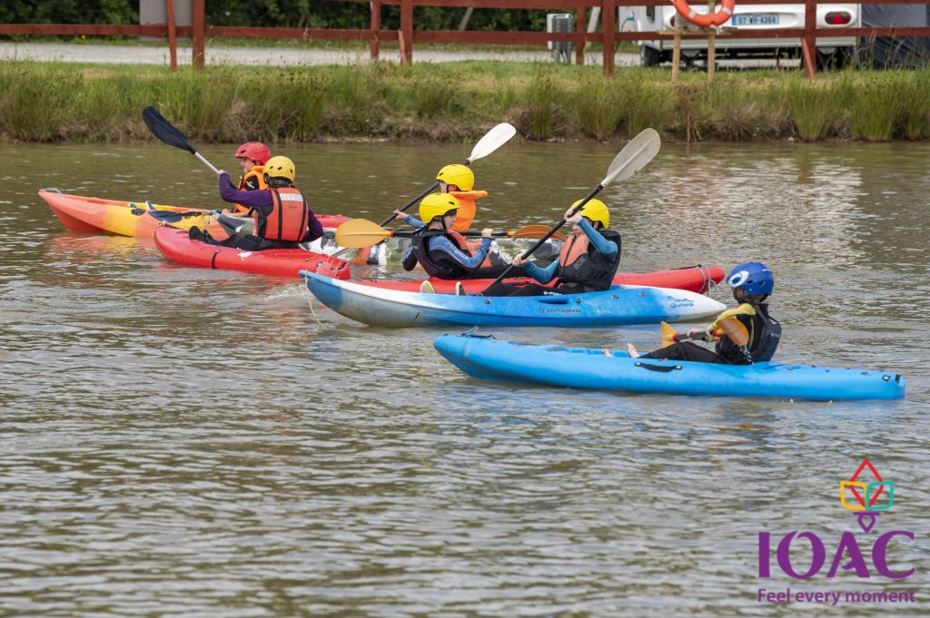 Four people kayaking in calm water wearing helmets and life jackets.