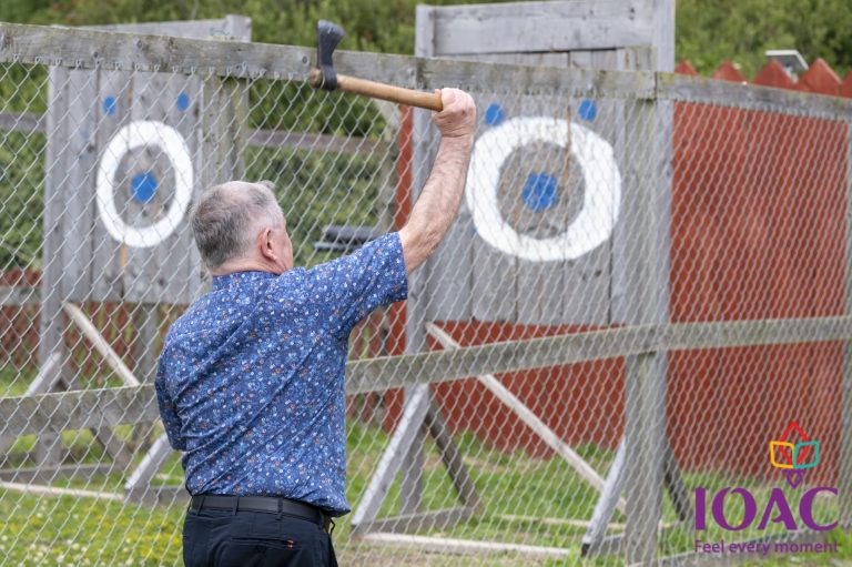 Man in blue shirt throwing an axe at a wooden target outdoors.