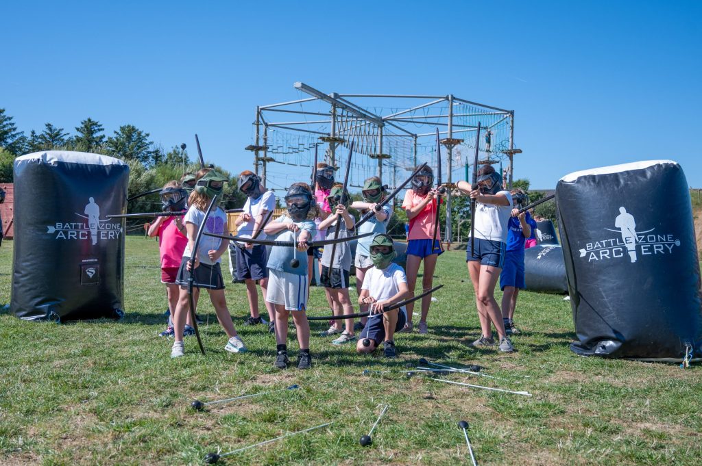 Group of kids with bows and arrows playing outdoors.