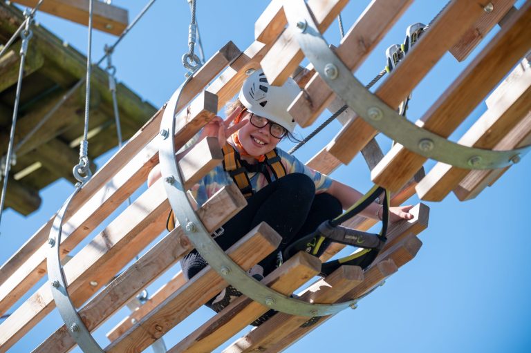 Person wearing a helmet navigates a wooden obstacle course mid-air.