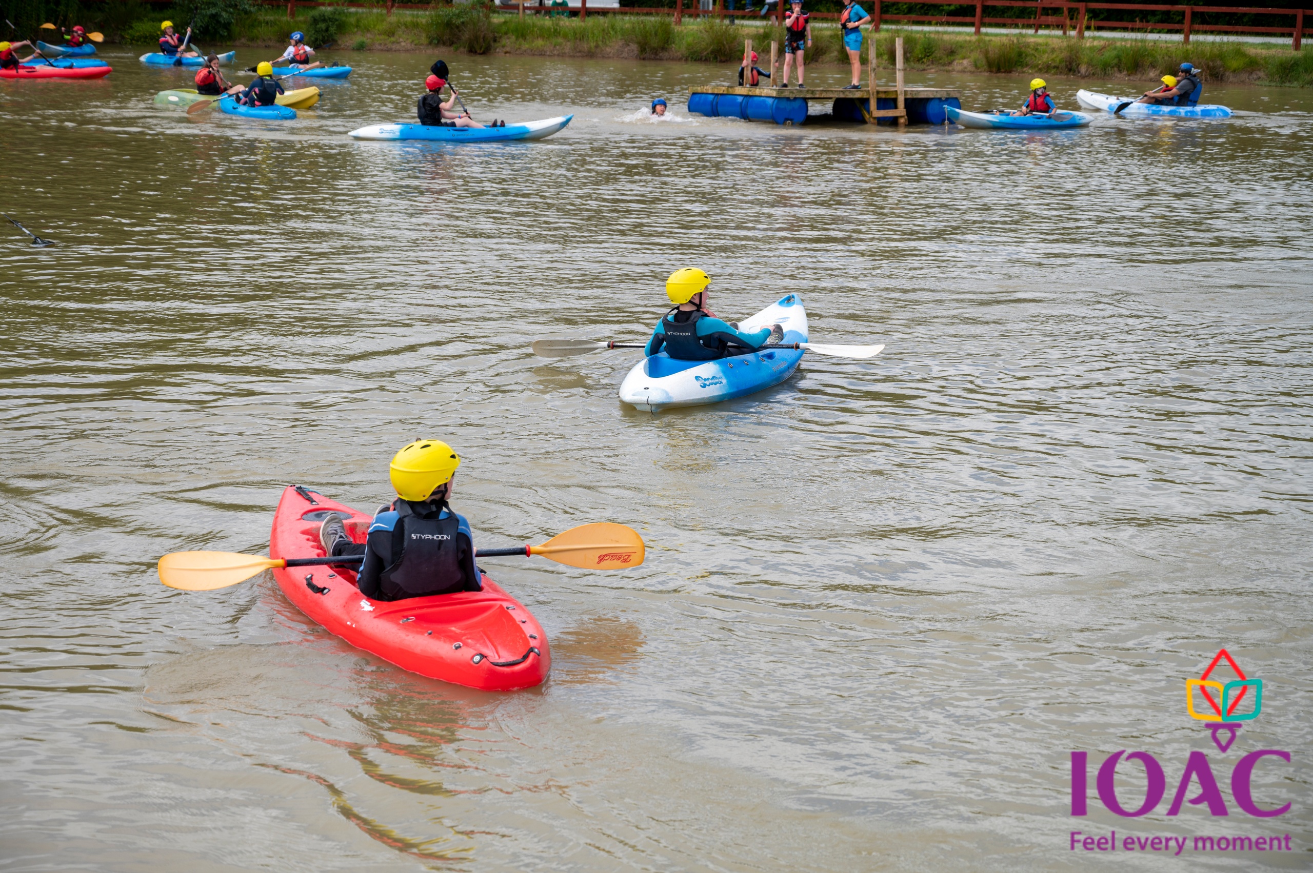 People kayaking on a lake wearing helmets and life vests.