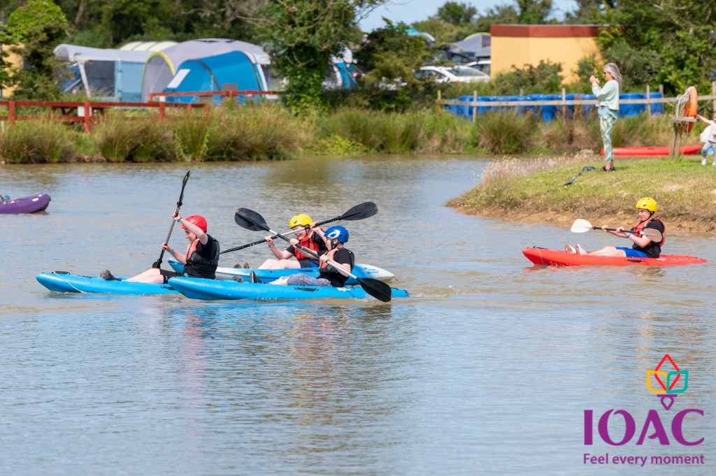 Four people kayaking in a pond near a campsite on a sunny day.