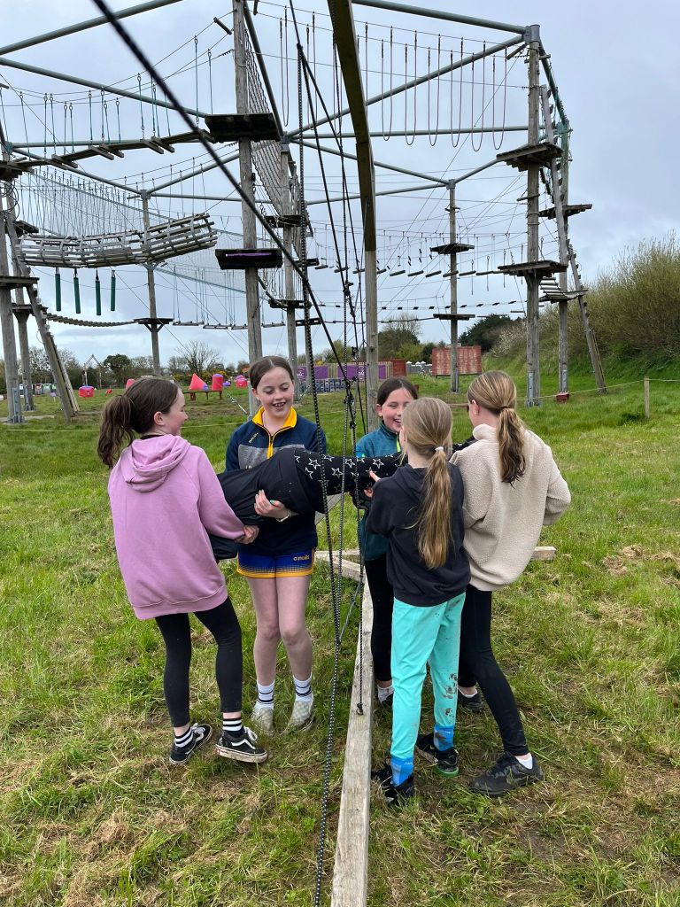 Five kids work together on a grassy field near a ropes course.