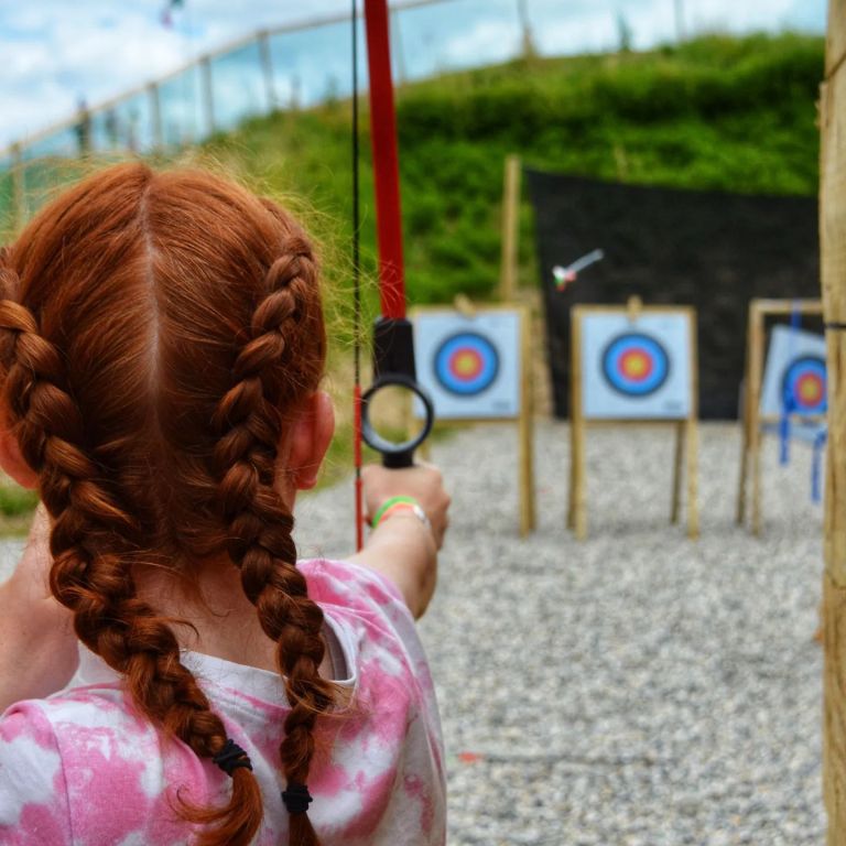 Child aiming a bow at archery targets outdoors.
