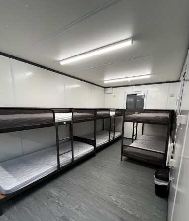 Clean, minimal room with four metal bunk beds and a trash bin.