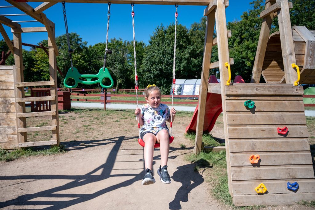 Child on a swing in a playground with climbing wall feature.