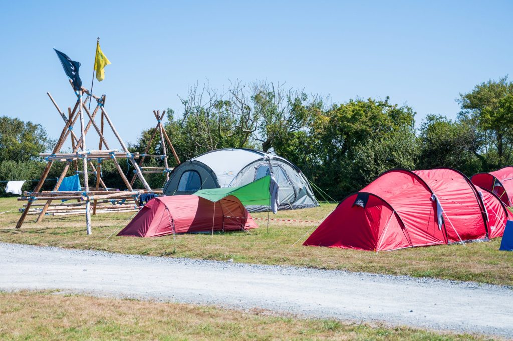 Campsite with red and gray tents, flags, and green grass.