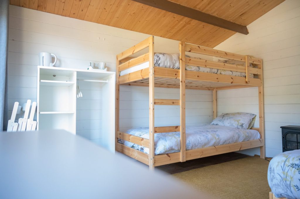Wooden bunk bed in a bright room with shelves and a small stove.
