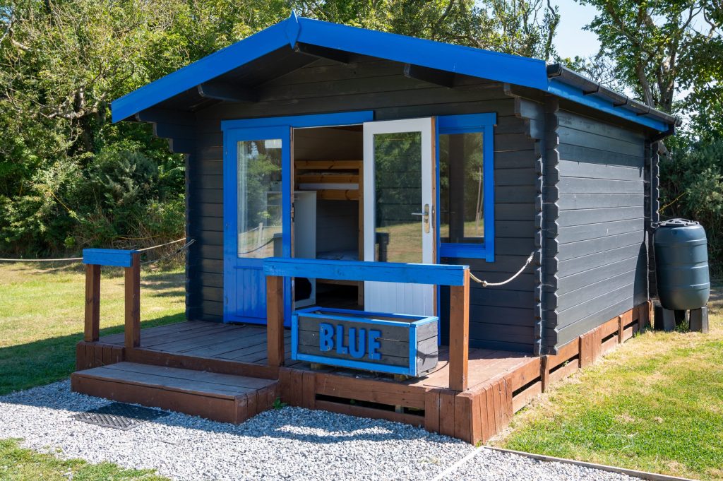 Small blue cabin with wooden porch in a grassy area.