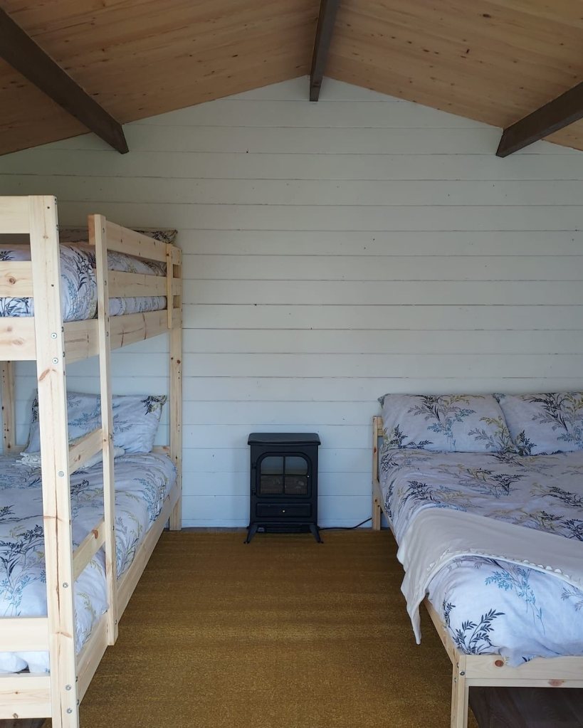 Room with bunk bed, double bed, and small heater on yellow carpet.
