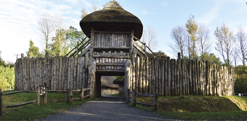 Medieval wooden fort with a thatched roof and surrounding palisade.