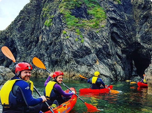 Group kayaking near rocky cliffs with orange paddles.