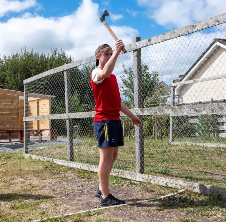 Person holding an axe, standing near a fence.