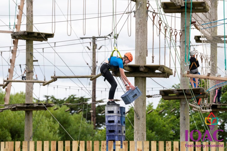 Person stacks crates while balancing on an outdoor ropes course.