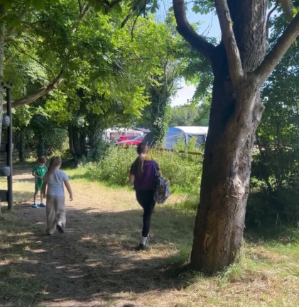 Two people walking on a forest path with sunlight filtering through trees.