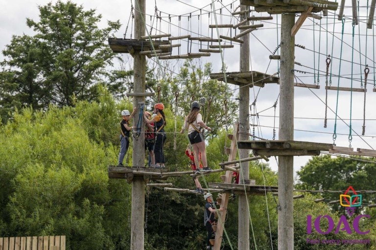Group of people on a high ropes course outdoors, wearing helmets.