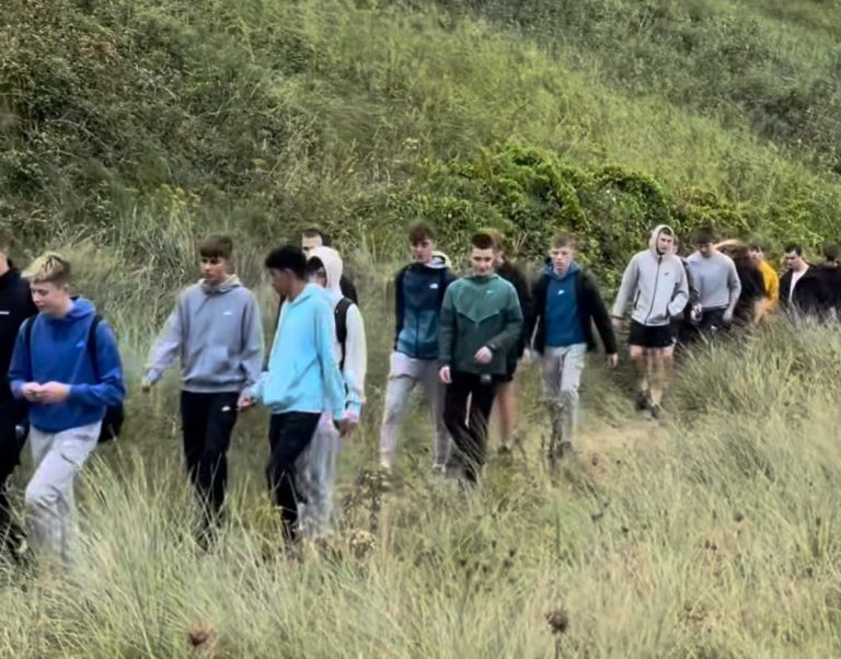 Group of people walking along a grassy hillside path.